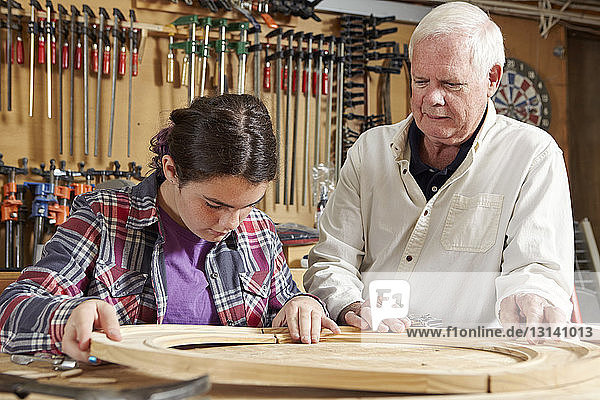Carpenter teaching girl in workshop