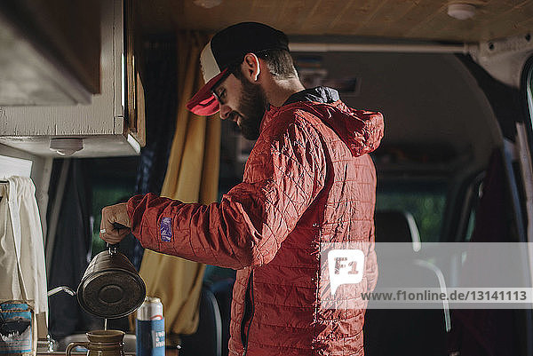 Side view of man making drink while standing in motor home