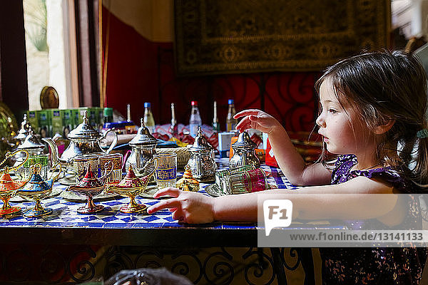 Side view of girl with magic lamps and teapots on table at home