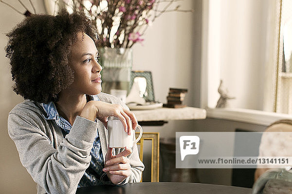 Woman with mug looking away while sitting at table