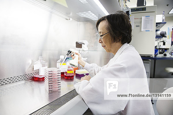 Side view of senior female scientist using pipette during experiment in laboratory