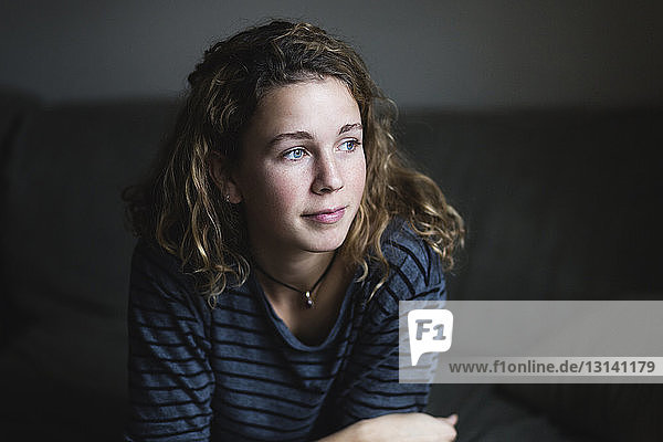 Thoughtful woman looking away while relaxing on sofa at home