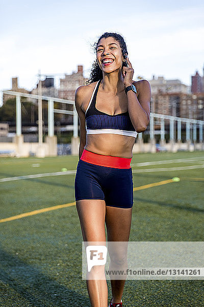 Glückliche Sportlerin spricht durch Kopfhörer  während sie auf Grasfeld läuft