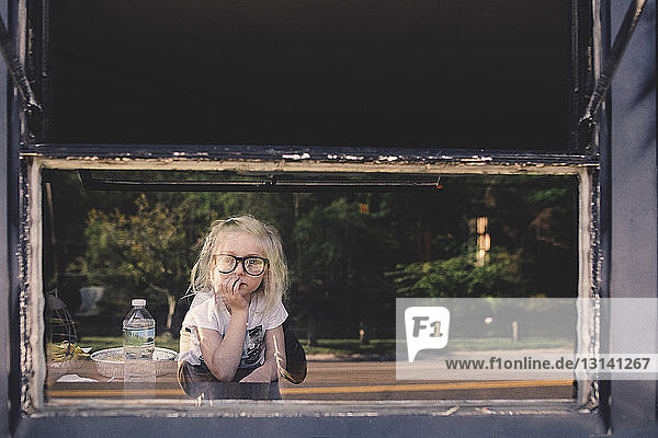 Thoughtful girl wearing eyeglasses leaning on table seen through glass