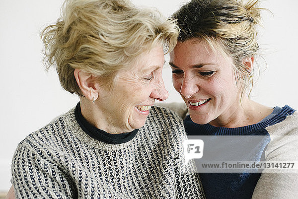 Close-up of affectionate mother and daughter sitting against wall at home