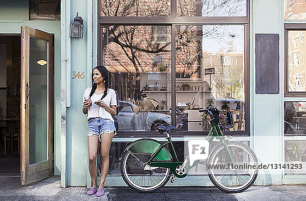 Nachdenkliche Frau steht mit dem Fahrrad vor dem Gebäude