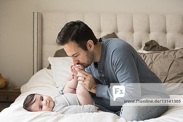 Father kissing son's feet while sitting on bed at home