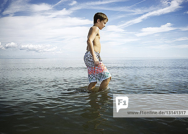 Seitenansicht eines Jungen ohne Hemd  der im Meer gegen den Himmel läuft
