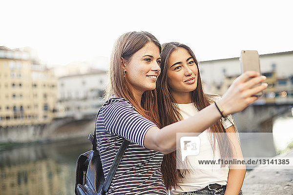 Lächelnde Freunde nehmen sich mit Smartphone gegen Kanal in der Stadt