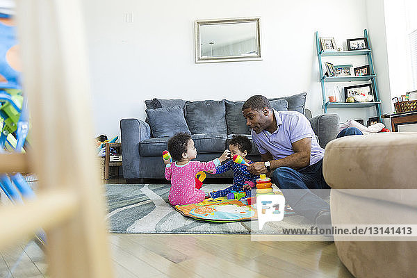 Vater spielt mit Töchtern  während er zu Hause auf dem Teppich sitzt