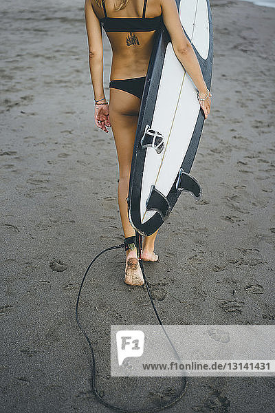 Niedriger Abschnitt einer Frau  die beim Strandspaziergang ein Surfbrett trägt