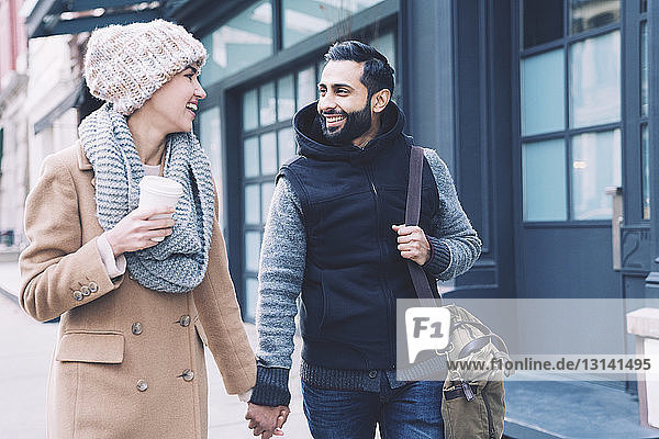 Glückliches Paar hält sich beim Spaziergang auf einem Fußweg in der Stadt an den Händen