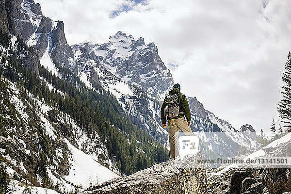Rear view of hiker standing on rock against snowcapped mountain