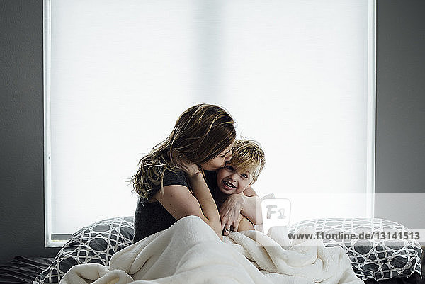 Portrait of boy with mother sitting on bed at home