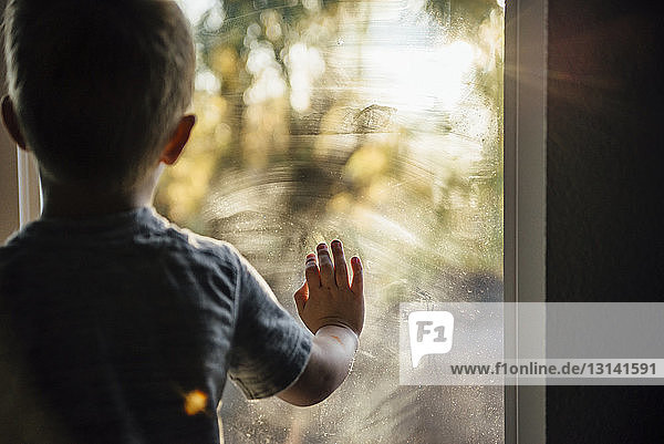 Rückansicht eines Jungen  der zu Hause durch ein Fenster schaut