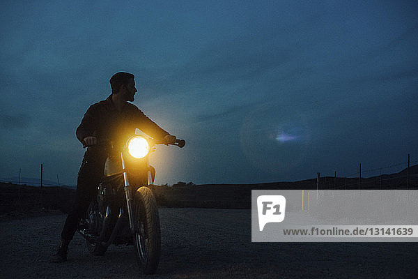 Low angle view of man riding illuminated motorcycle on street at dusk