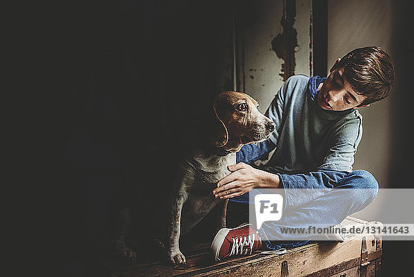 Teenage boy with dog sitting on wooden box in darkroom at home