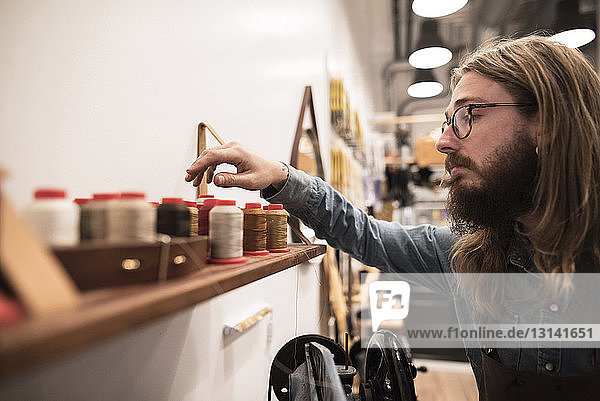 Shoemaker choosing spool on shelf at workshop
