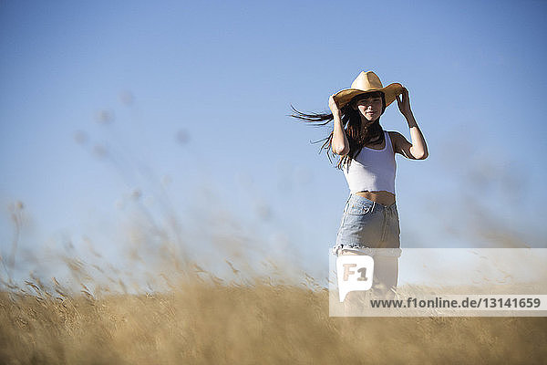 Porträt einer Frau mit Cowboyhut  die auf einem Feld gegen den Himmel steht