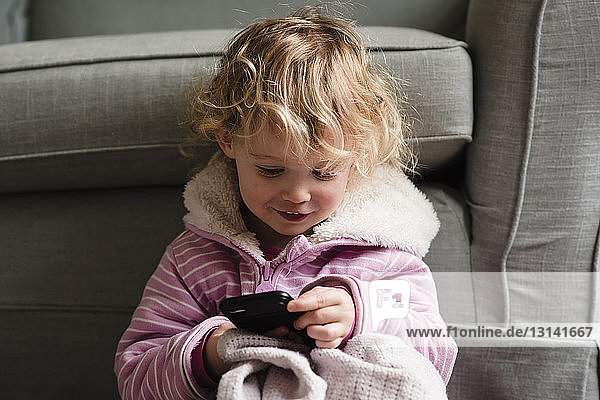 Girl using mobile phone while sitting by armchair at home