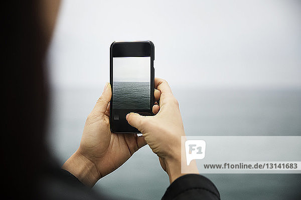 Ausschnitt einer Frau  die mit ihrem Mobiltelefon das Meer fotografiert