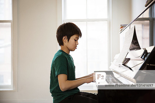 Seitenansicht eines Jungen  der zu Hause Klavier spielt