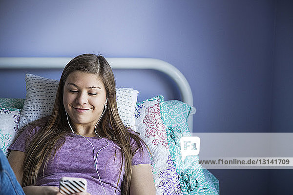 Lächelndes Mädchen benutzt Smartphone beim Entspannen im Bett
