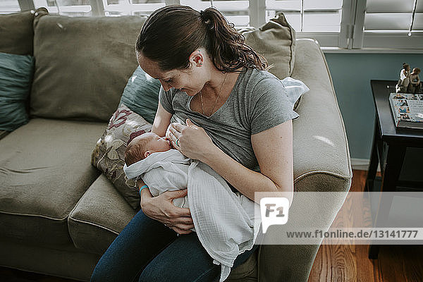 High angle view of mother breastfeeding newborn son while sitting on sofa at home
