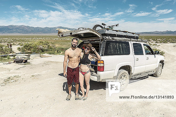Hochwinkel-Porträt eines Paares in Badebekleidung  das an einem sonnigen Tag in Spencer Hot Springs gegen ein Geländefahrzeug steht
