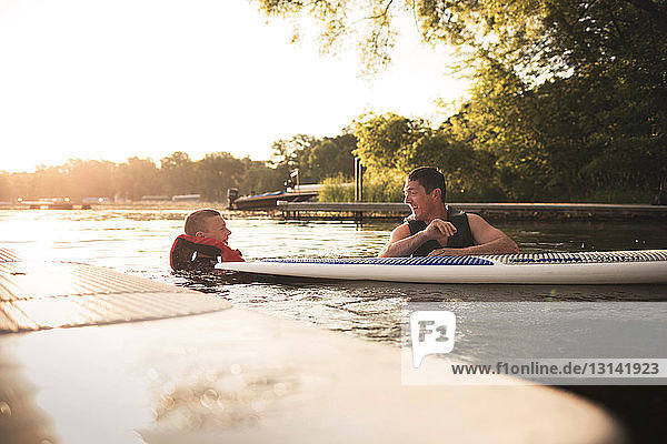 Glückliche Vater und Sohn schwimmen mit dem Paddelbrett auf dem See