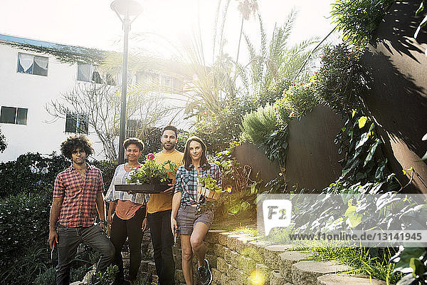 Portrait of confident friends holding potted plants in community garden