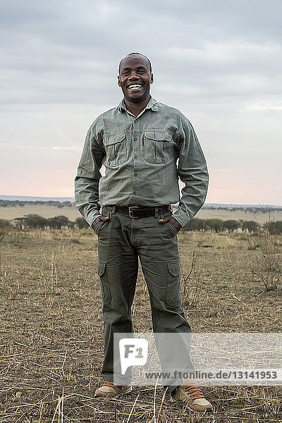 Porträt eines glücklichen Mannes  der auf einem Grasfeld im Serengeti-Nationalpark steht
