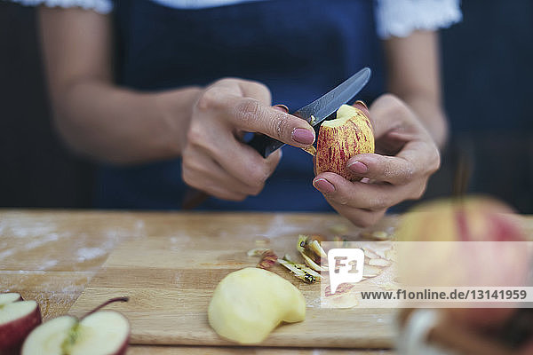 Nahaufnahme von Frauenhänden beim Apfelschneiden für die Zubereitung der Zimtschnecke zu Hause