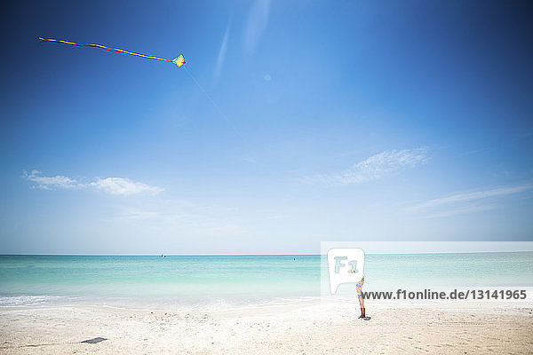 Girl flying kite at beach against sea and sky