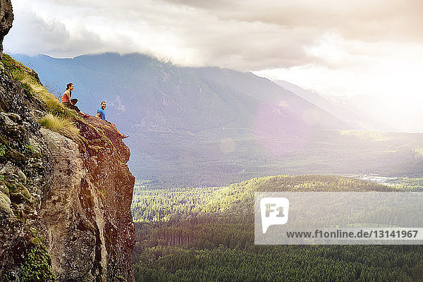 Seitenansicht eines Paares  das auf einer Klippe gegen einen Berg sitzt