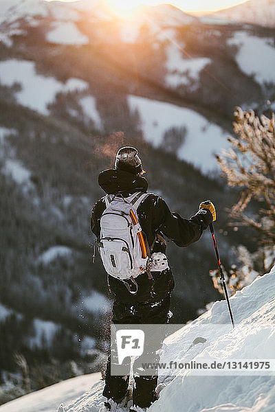 Rear view of man with skies standing on snow covered mountain during sunset