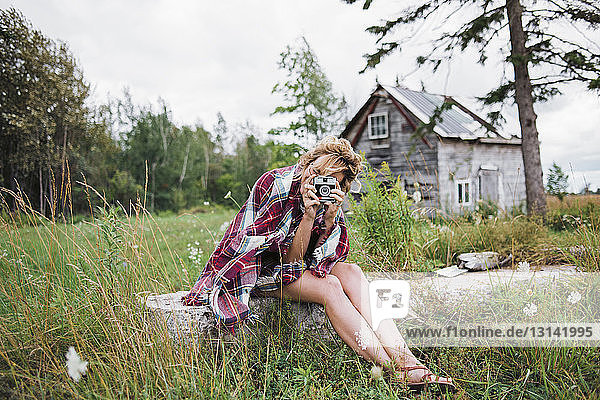 Frau fotografiert mit Sofortbildkamera  während sie auf einem Grasfeld sitzt
