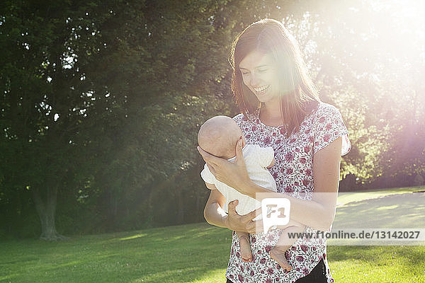 Glückliche Mutter  die an einem sonnigen Tag im Park steht und ihr Kind austrägt
