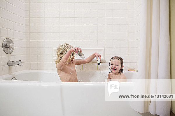 Shirtless sisters playing while bathing in bathtub at home