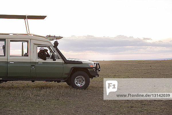 Mann schaut durch ein Fernglas  während er im Geländewagen im Serengeti-Nationalpark sitzt