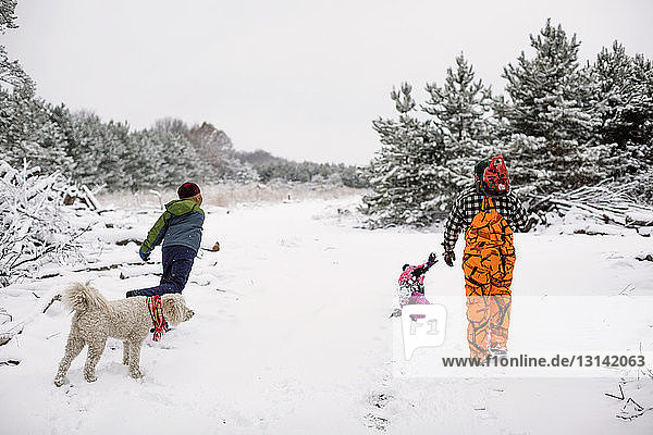 Playful family enjoying on snow covered field against sky