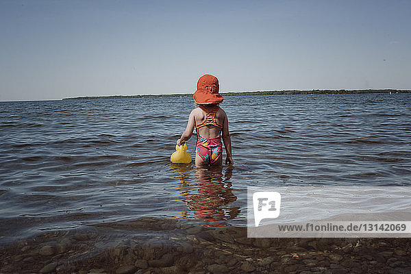 Rückansicht eines Mädchens mit Gummiente im Meer vor klarem Himmel an einem sonnigen Tag
