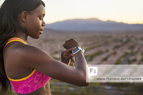 Side view of female athlete checking wristwatch against village