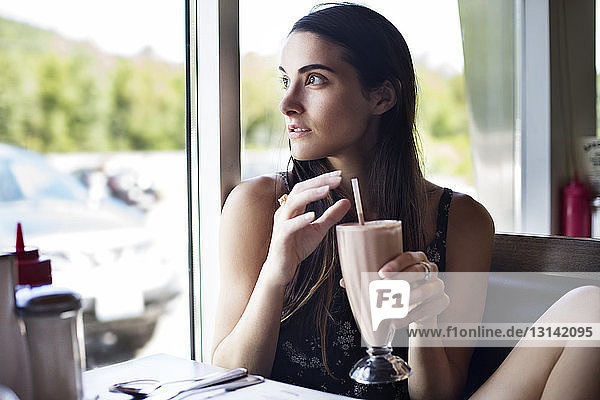 Frau schaut weg  während sie einen Schoko-Milchshake im Café hält