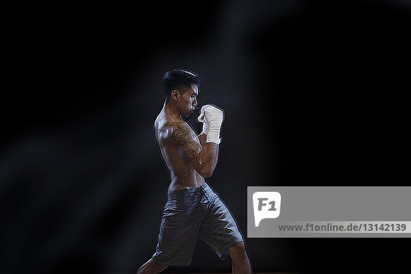 Seitenansicht eines männlichen Kickboxers  der vor schwarzem Hintergrund kämpft