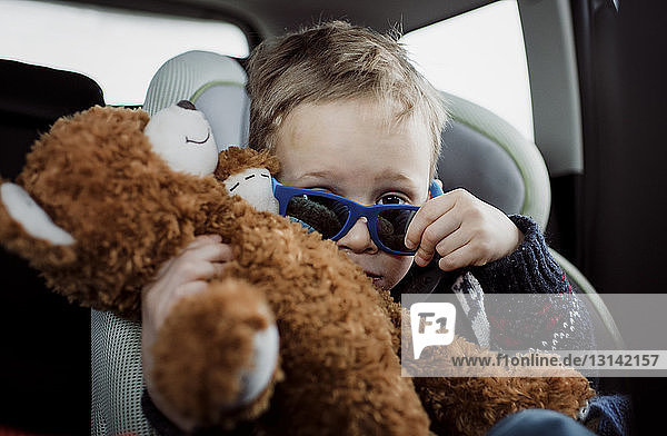 Portrait of boy with stuffed toy wearing sunglasses while sitting in car