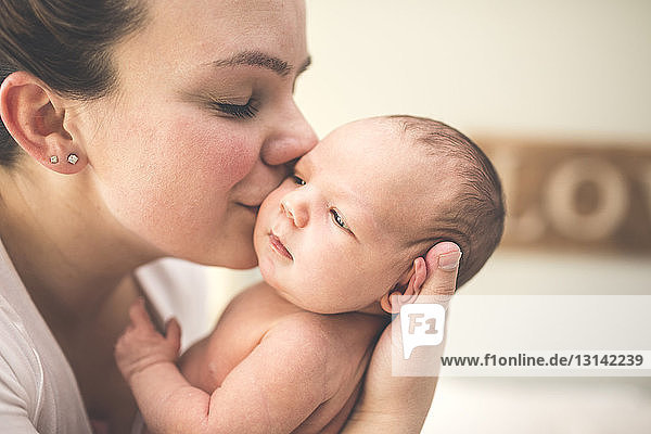 Seitenansicht einer Mutter  die ihre neugeborene Tochter zu Hause küsst