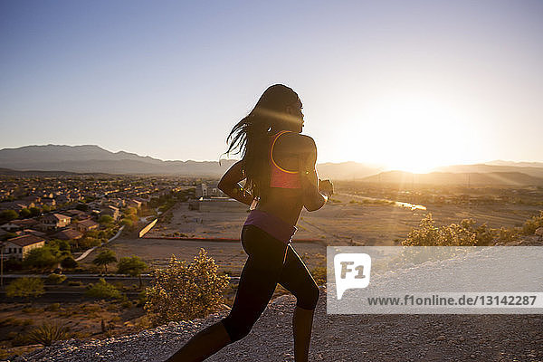 Weibliche Athletin joggt an einem sonnigen Tag auf unbefestigter Straße vor klarem Himmel