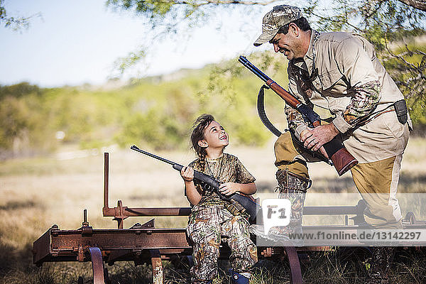 Vater und Tochter lächeln sich an  während sie das Gewehr halten