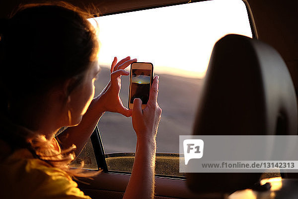 Frau im Auto fotografiert den Himmel bei Sonnenuntergang